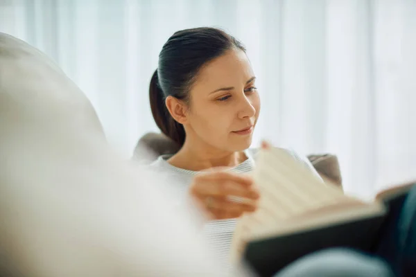 Young woman relaxing on the sofa and reading a book.