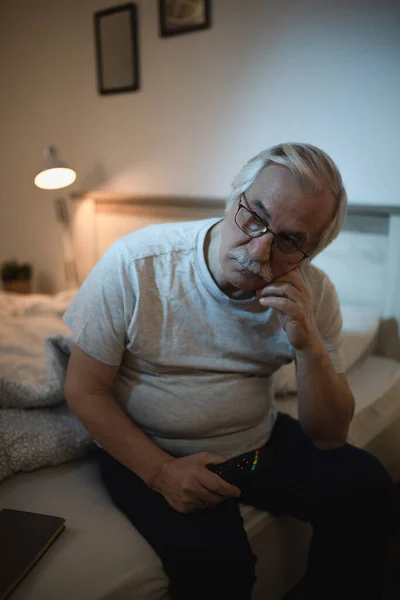 Pensive senior man thinking of something while sitting awake late at night in bedroom.