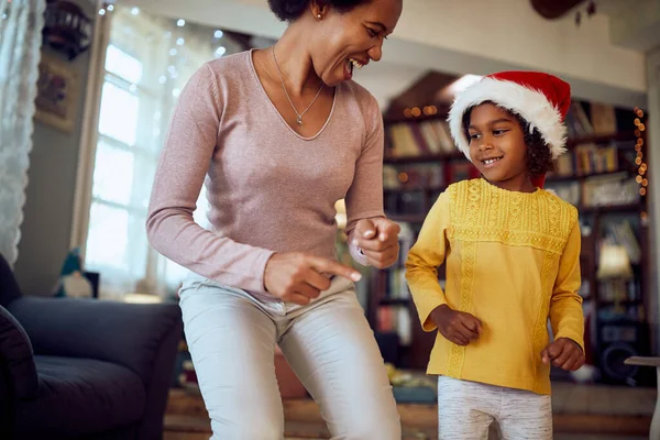 Happy African American mother and daughter dancing and having fun on Christmas at home.