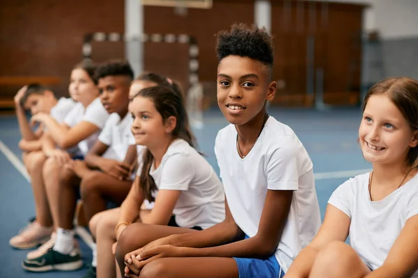 Multi-ethnic group of elementary students having physical activity class at school. Focus is on happy black boy looking at camera.