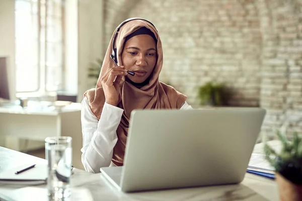Black Muslim Customer Service Representative Talking Her Client While Working — стоковое фото