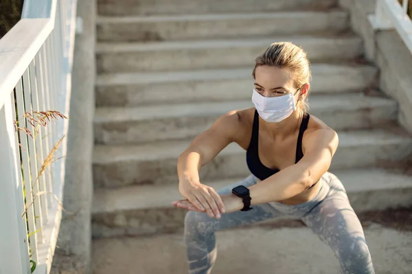 Athletic woman with face mask exercising squats during sports training outdoors.