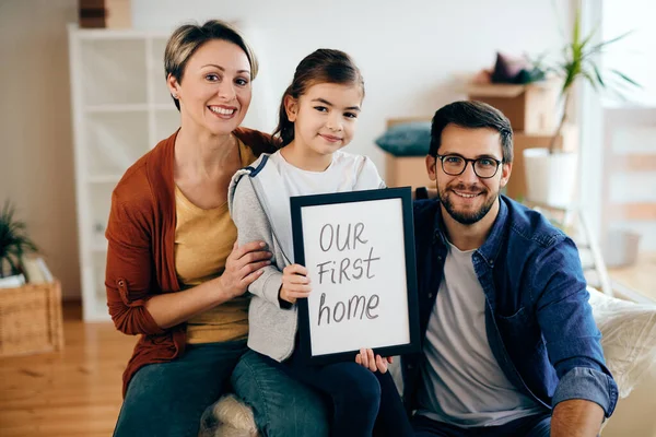 Happy family holding picture frame with \'our new home\' inscription while moving into a new house.
