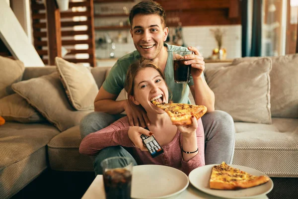 Young happy couple watching movie on TV and eating pizza in the living room.