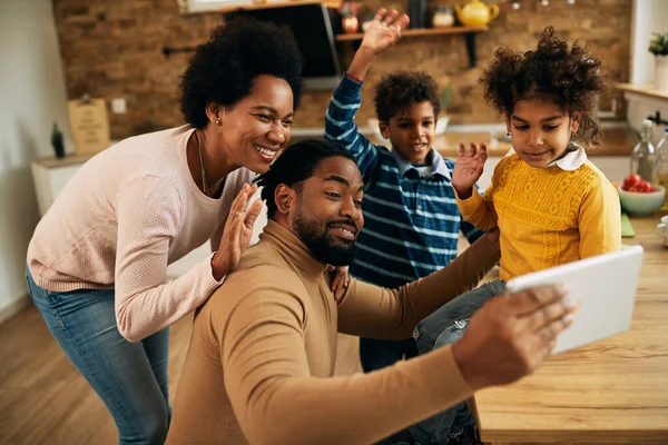 Happy black family having fun while making video call over touchpad and waving to someone.