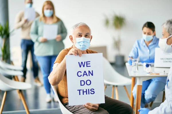 Senior man with face mask getting vaccinated against coronavirus and showing placard with \