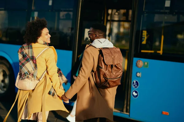 Happy African American couple talking while holding hands and walking toward a bus on the station.