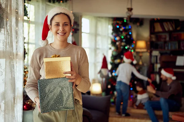Happy Mother Holding Christmas Gifts While Her Family Background Home — ストック写真