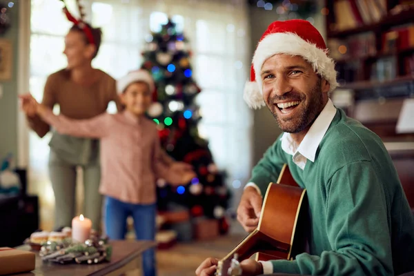Happy Man Wearing Santa Hat Playing Acoustic Guitar His Wife — ストック写真