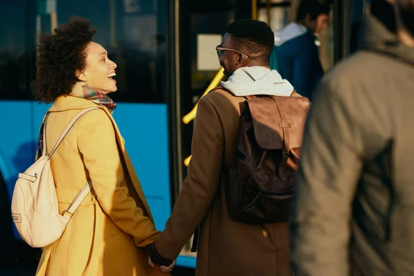 Happy black woman communicating with her boyfriend while holding hands with is at bus station.