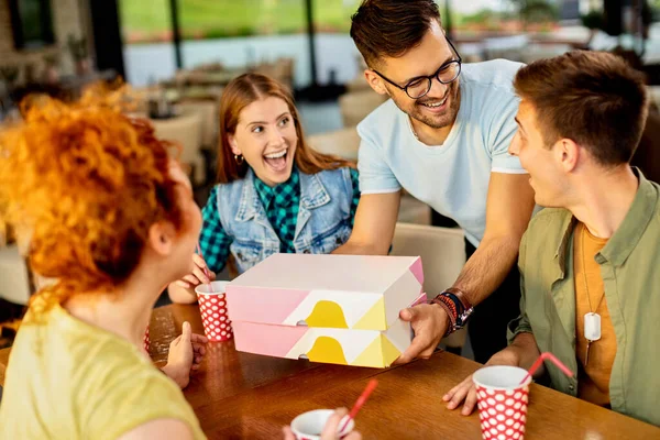 Happy man having fun while surprising his friends with box of donuts in a cafe,
