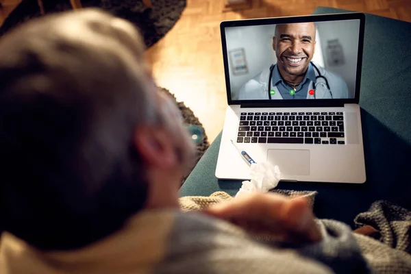 Close-up of a man having video call over laptop with his doctor in the evening at home. Focus is on African American doctor on laptop screen.