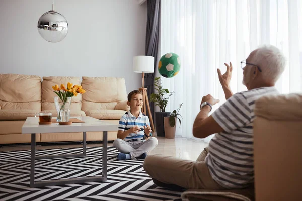 Happy grandfather and grandson having fun and playing with ball at home. Focus is on boy. 