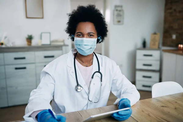 Black female doctor using digital tablet while wearing face mask and working at the clinic.