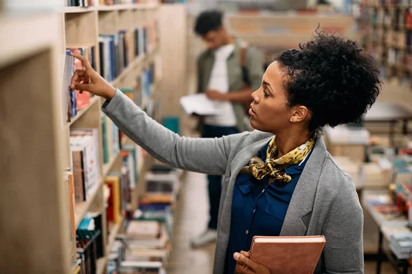 Mid Adult Black Woman Searching Books Bookshelf While Studying Library — Stockfoto