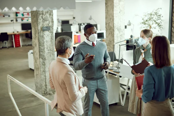 African American business leader talking to his team during the briefing in the office. They are wearing protective face masks due to coronavirus pandemic.