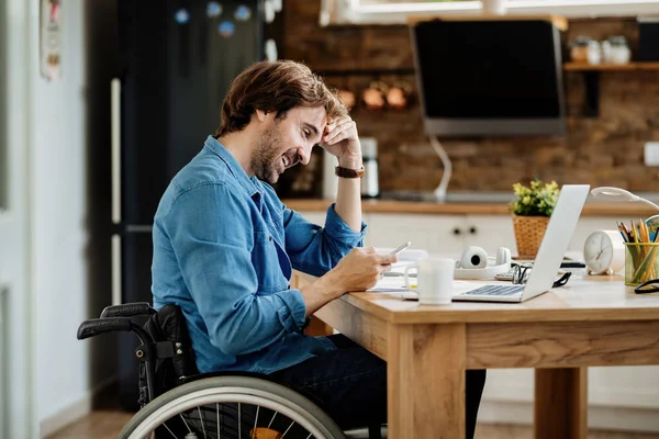 Young happy businessman in wheelchair working at home and text messaging on mobile phone.