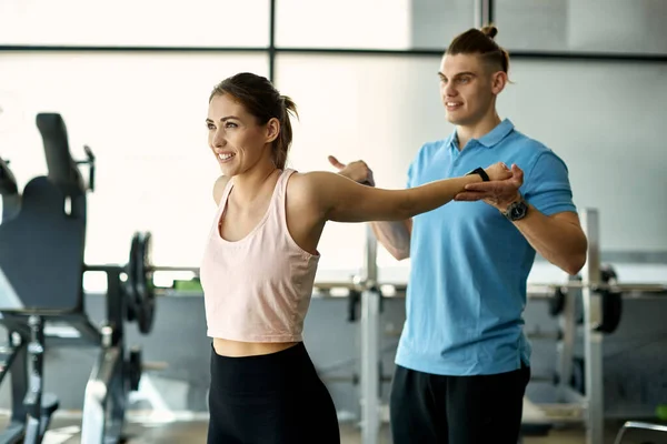 Male coach stretching woman\'s arms after sports training in a gym.