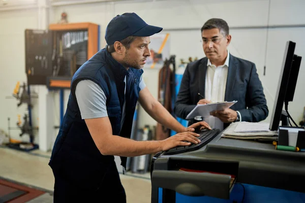 Mid Adult Inspector Overseeing Auto Repairman Who Working Computer Workshop — ストック写真