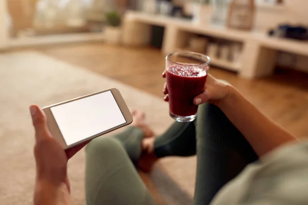 Close-up of athletic woman drinking fruit smoothie and using mobile phone at home. Copy space.