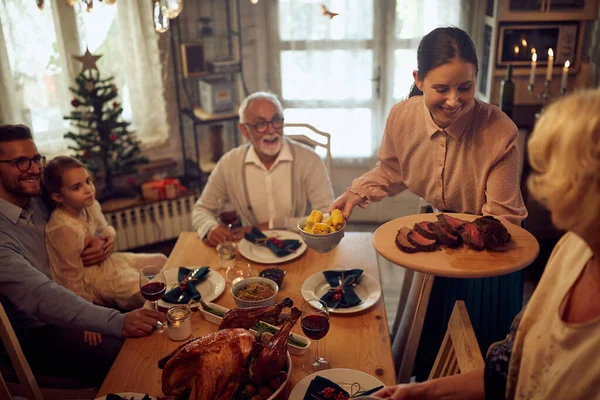 Happy woman celebrating Thanksgiving with her extended family and bringing food at the table.