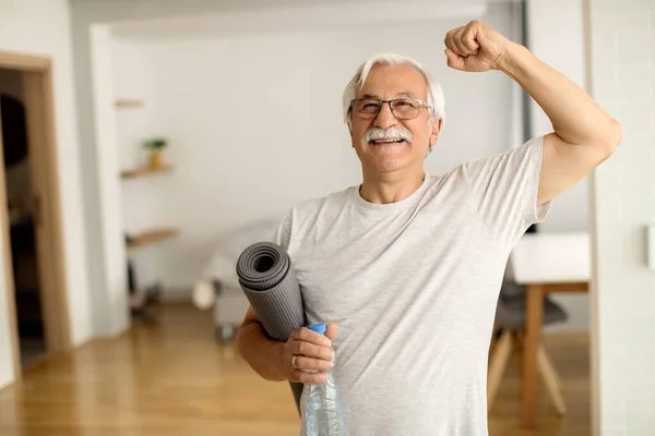 Happy senior man celebrating with raised arm after working out at home.