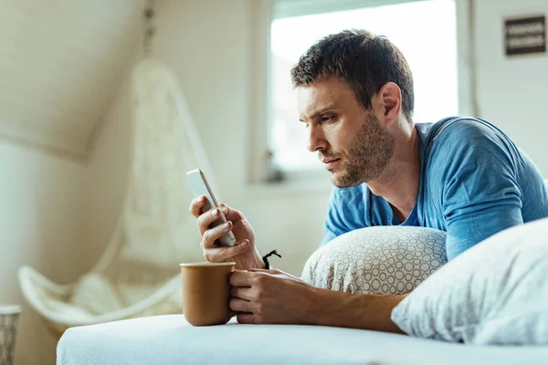 Young Man Lying Bed Drinking Coffee While Text Messaging Mobile — Foto de Stock
