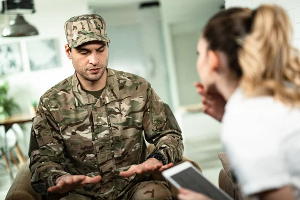 Young military man gesturing while showing physiological tremor symptoms to a doctor who is visiting him at home. 