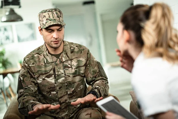 Young military man gesturing while showing physiological tremor symptoms to a doctor who is visiting him at home.
