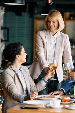 Happy businesswoman toasting with wine while having lunch with colleagues in a restaurant. 