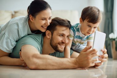 Happy parents with son using touchpad and taking selfie at home. 