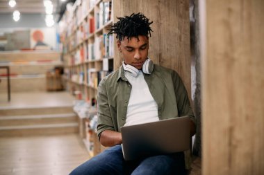 African American male student using laptop while learning at university library. 