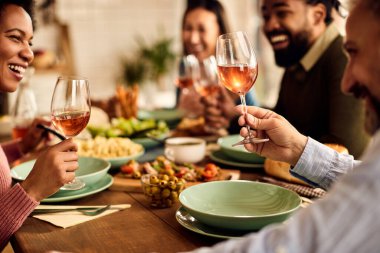 Close-up of multi-ethnic group of friends drinking wine while eating together at dining table. 