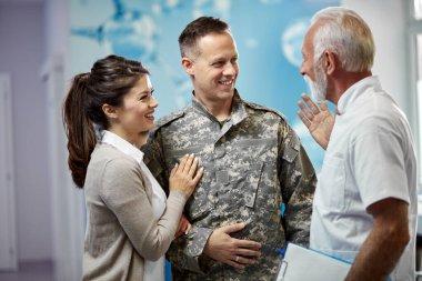 Happy officer and his wife communicating with senior doctor while standing in a hallway at medical clinic. 