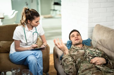 Young healthcare worker listening to military man who is lying down on sofa and talking to her. 
