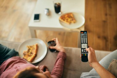 Close-up of couple changing channels on TV while eating pizza at home.