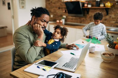 African American stay at home father trying to work on laptop while being distracted by his small daughter. 