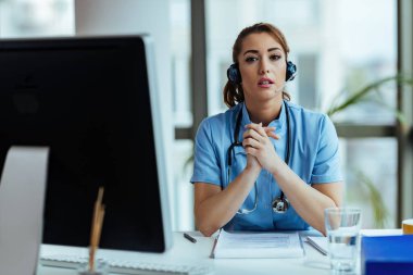 Young female doctor with headset providing support and communicating with patients while working in medical call center. 