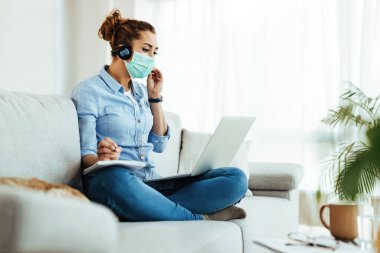 Young woman female student writing notes while following online classes over laptop at home during coronavirus epidemic. 