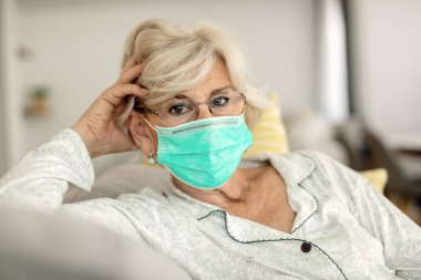 Mature woman with protective face mask sitting at home and looking at camera. 