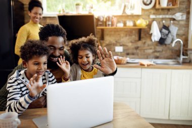 Mutlu Afrikalı Amerikalı baba ve çocukları evde bilgisayar kullanırken el sallıyor ve video görüşmesi yapıyor.. 