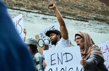 Low angle view of black protester with raised fist shouting through megaphone on anti-racism demonstrations. 