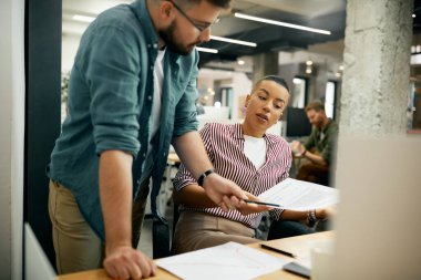 African American entrepreneur and her male colleague going through business reports while working in the office.