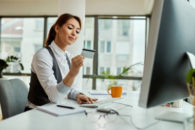Smiling businesswoman using credit card and computer while buying on the internet in the office. 