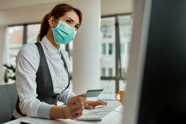 Businesswoman with face mask using computer and shopping on the internet with credit card in the office during COVID-19 pandemic. 