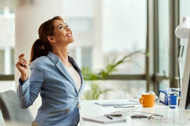 Happy female entrepreneur looking up while stretching in the office. 