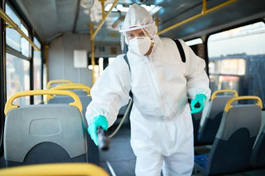 Sanitation worker in hazmat suit doing disinfection of public transportation due to COVID-19 epidemic. 