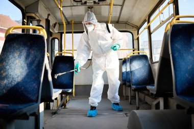 Sanitation worker in hazmat suit disinfecting city bus during COVID-19 epidemic.