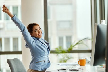 Happy businesswoman stretching while working on desktop PC in the office. 