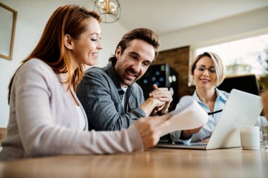 Low angle view of young happy couple having consultations with their financial advisor at home. Focus is on man. 